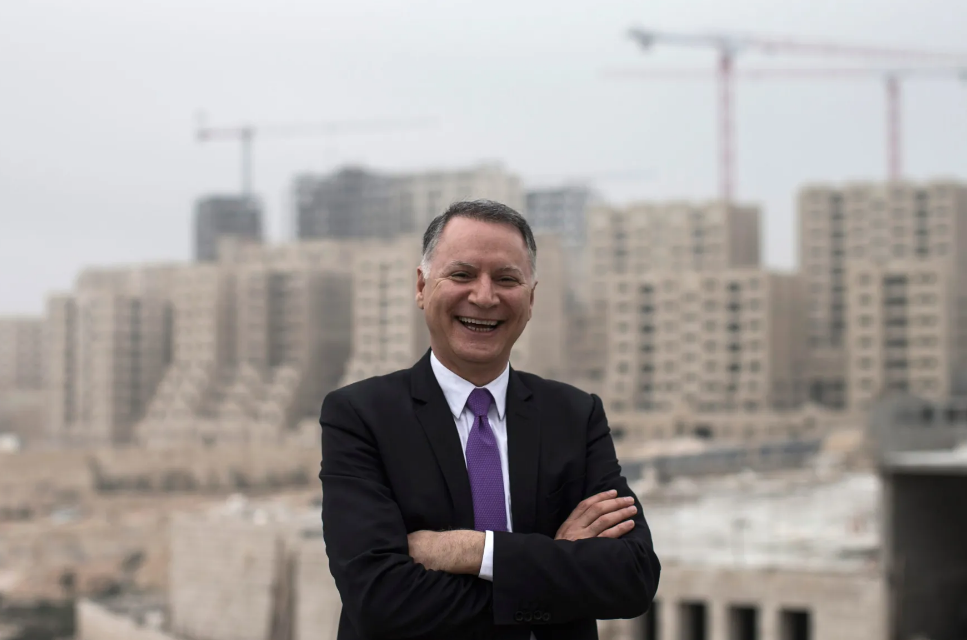 Bashar Masri smiling with his arms crossed in front of apartment buildings under construction in Rawabi City