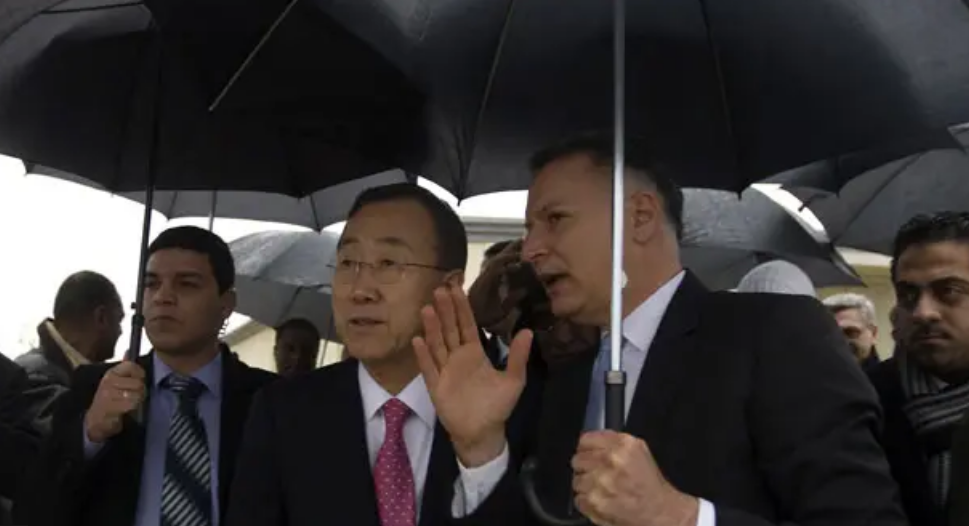 Bashar Masri speaking with Ban Ki-moon under umbrellas during a rainy visit to Rawabi City in 2012
